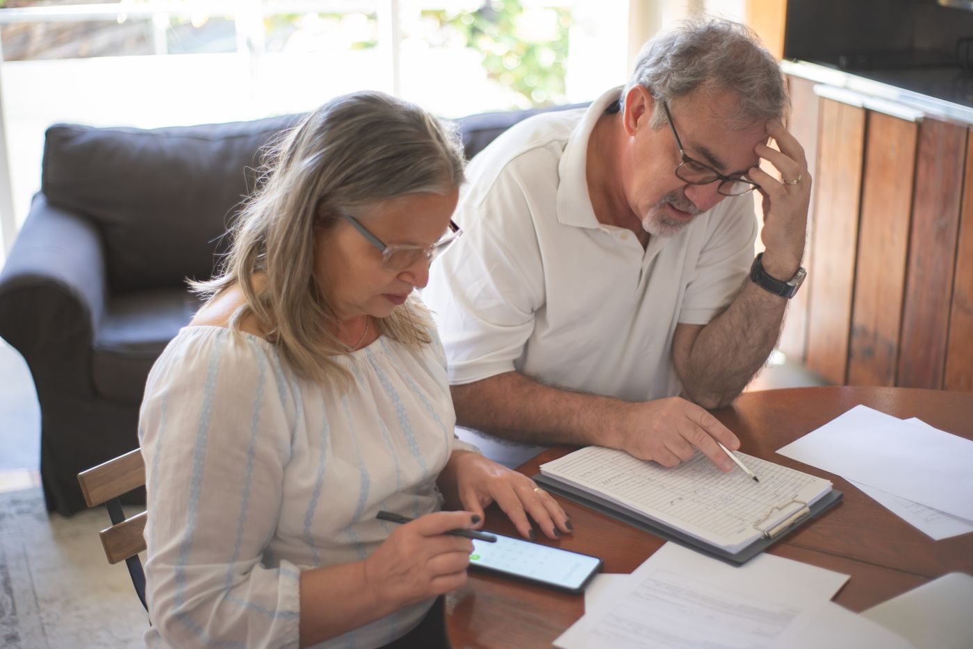 A Utah couple in their seventies sitting at a kitchen table sorting long-term care bills and tax paperwork with a calculator.