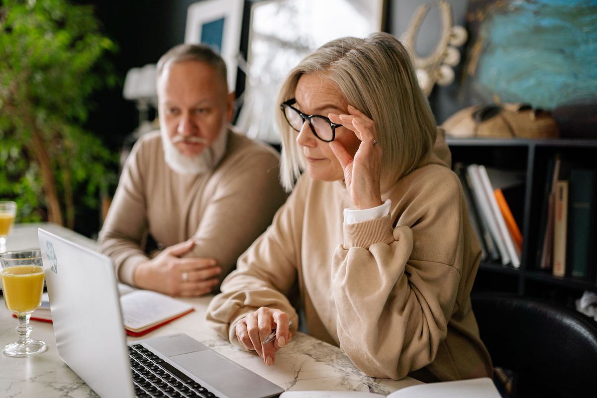 A retired couple sit at a marble table looking closely at a laptop, the woman adjusting her glasses as they compare 2027 Medicare plan star ratings.