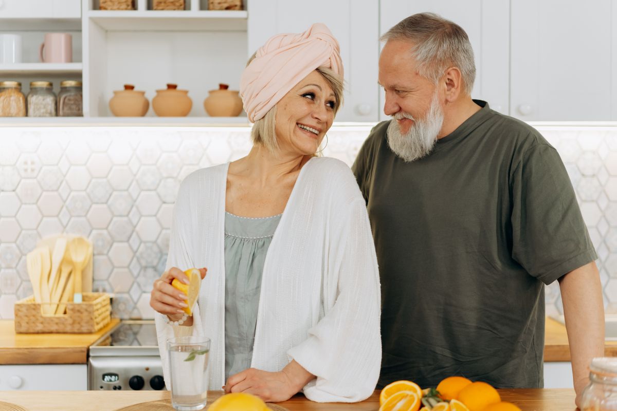 An older couple smile at each other in a bright kitchen as the woman squeezes lemon into a glass of water, the clear-liquid morning before a Medicare-covered screening colonoscopy for a Utah retiree.