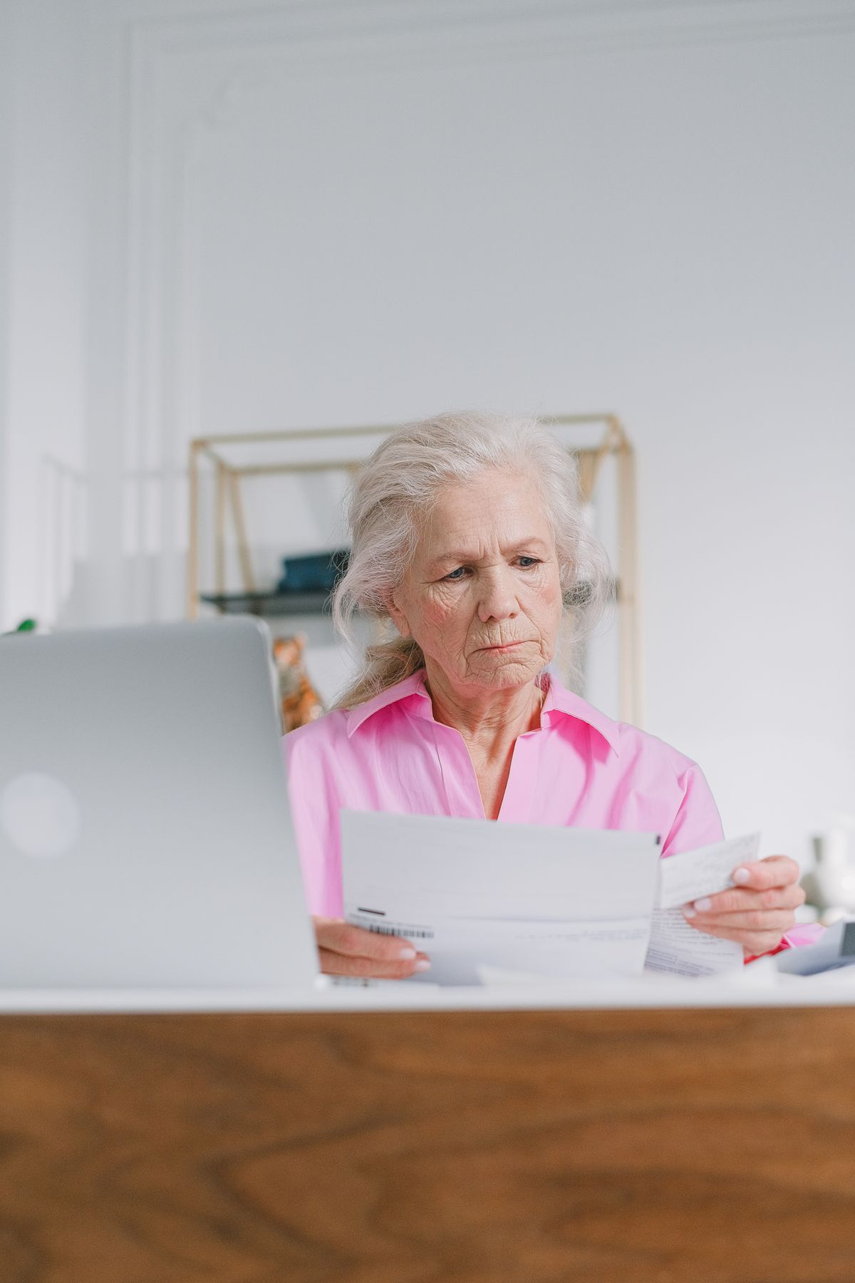 A gray-haired retired Utah public employee in a pink blouse reads pension paperwork at her desk beside a laptop, checking her Utah Retirement Systems benefit.