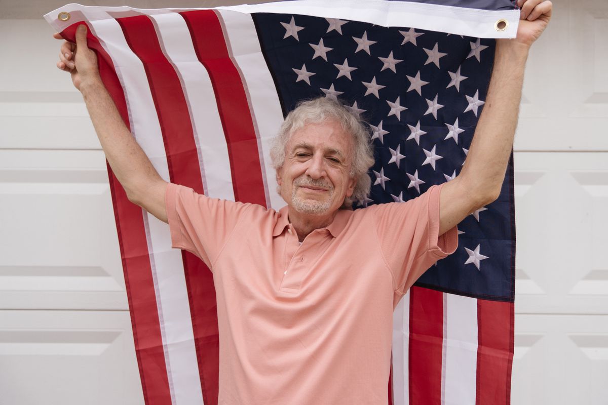 An older U.S. veteran holding a small American flag — the moment a Utah veteran turning 65 has to decide whether to add Medicare Part B to VA health care, TRICARE for Life, or CHAMPVA.